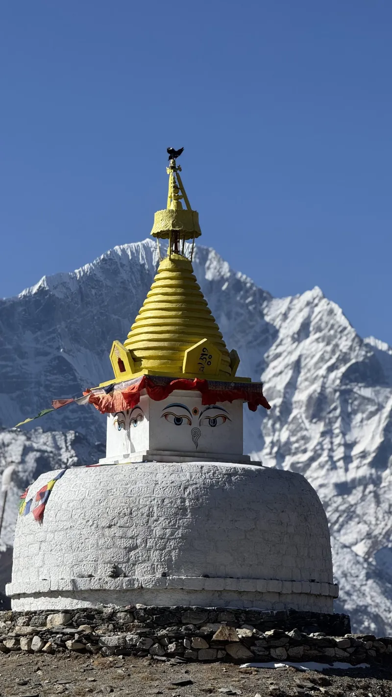 A Sherpa stupa with painted Buddha eyes and prayer flags, snow peaks rising behind it