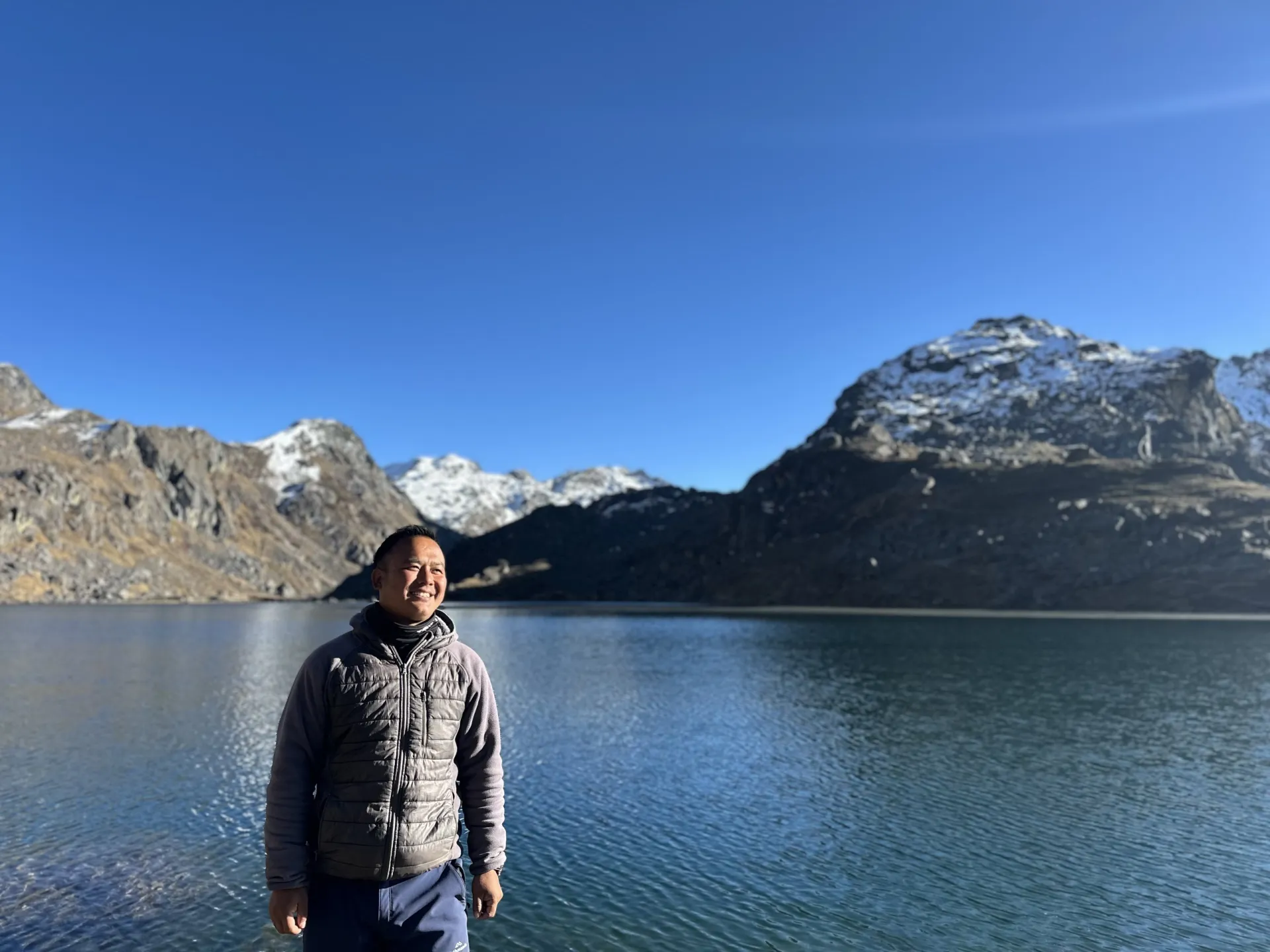 A guide standing beside the still, deep-blue water of the sacred alpine lake Gosaikunda
